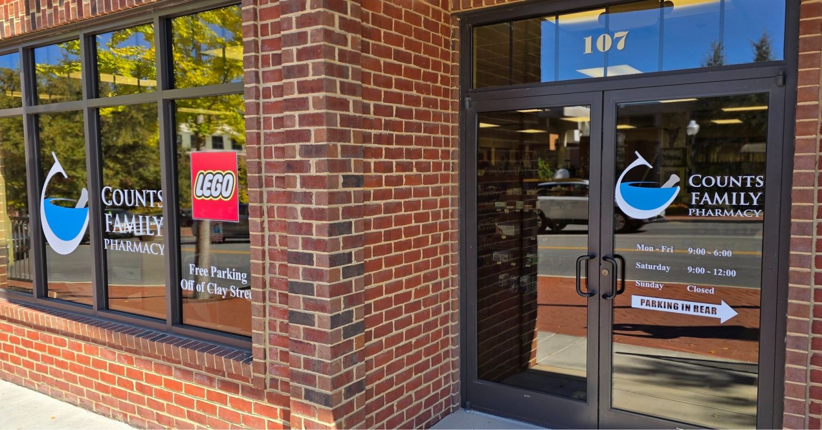 474196738_1446192100086597_4118506602286855879_n Counts Family Pharmacy storefront with glass windows and a LEGO sign, brick exterior, and business hours posted.
