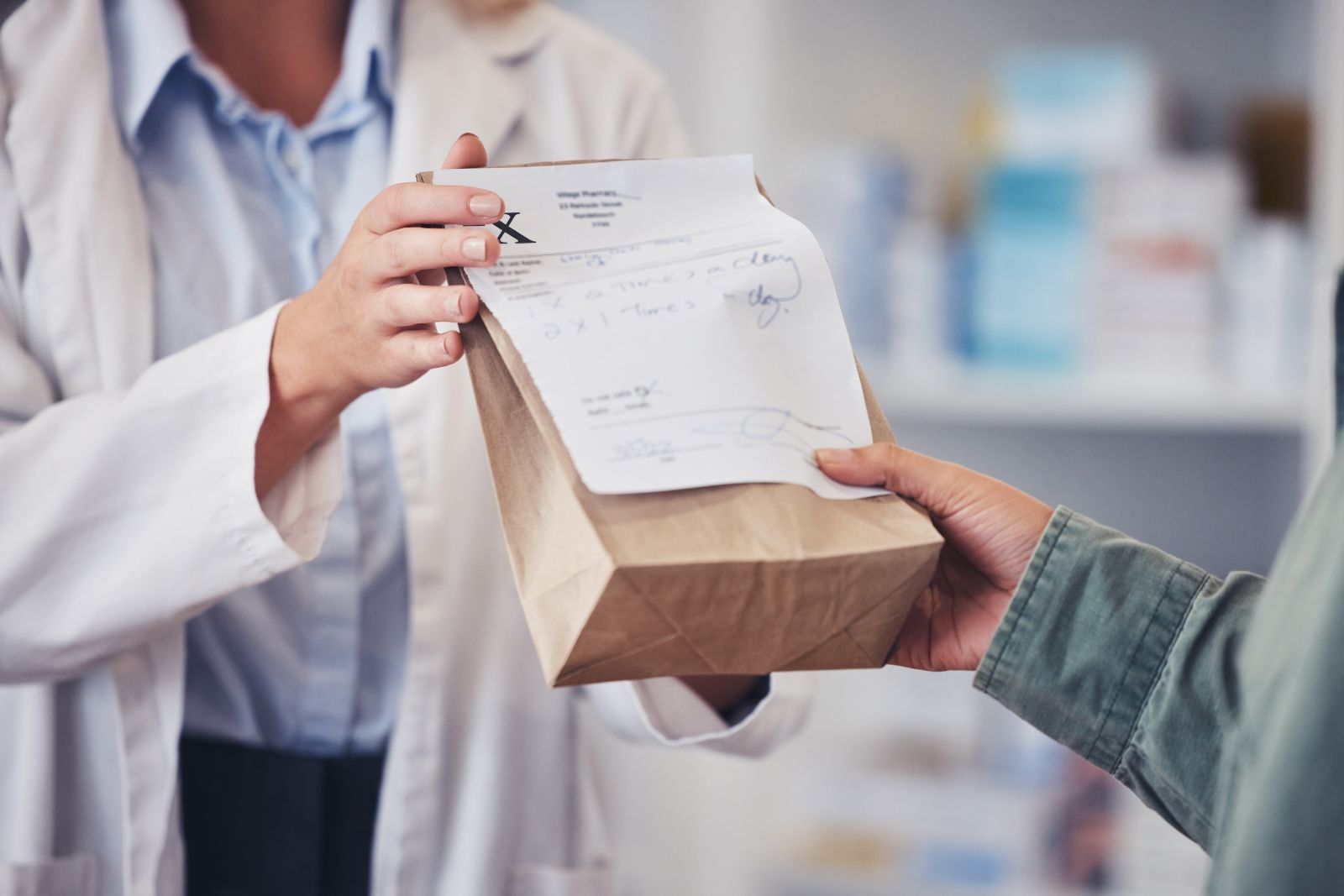 A pharmacist hands a paper bag with a prescription to a customer across the counter.