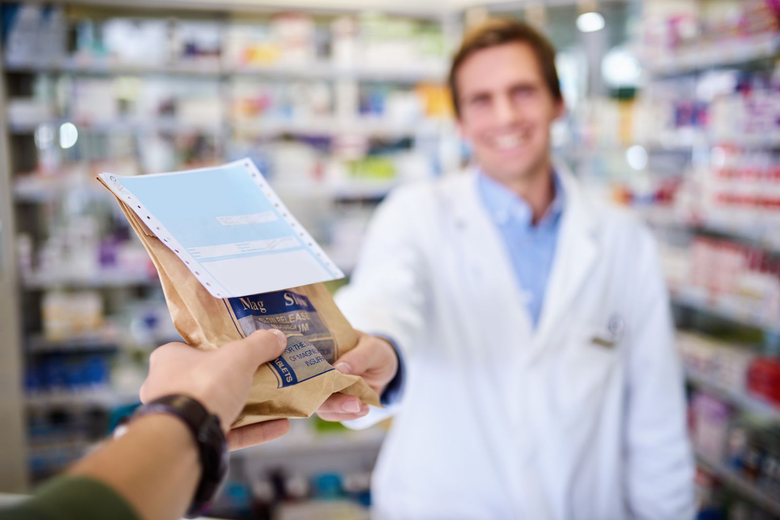 A pharmacist hands a paper bag with a prescription to a customer in a pharmacy.
