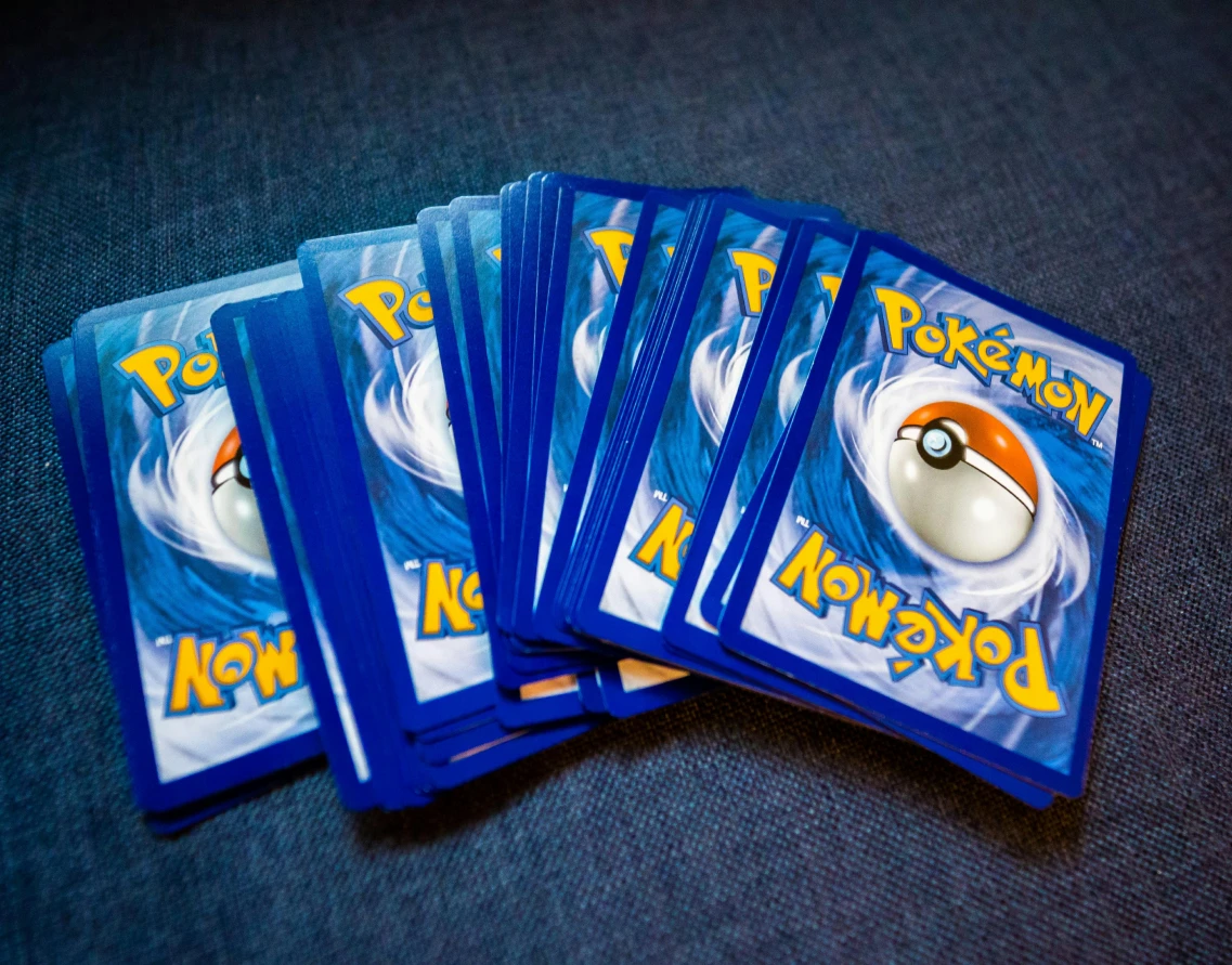 A spread of Pokémon trading cards with the card backs showing, arranged on a dark blue surface.